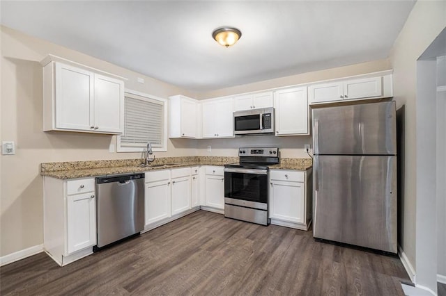 kitchen with white cabinets, appliances with stainless steel finishes, dark hardwood / wood-style floors, and light stone countertops