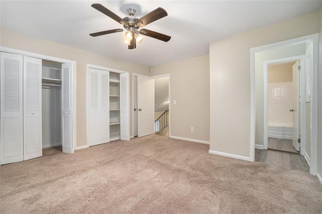 unfurnished bedroom featuring light carpet, ensuite bath, ceiling fan, and multiple closets