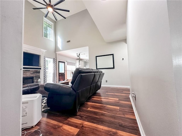 living room with a high ceiling, a ceiling fan, wood finished floors, baseboards, and a stone fireplace