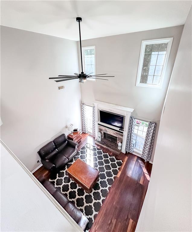living room with plenty of natural light, wood finished floors, a stone fireplace, and ceiling fan