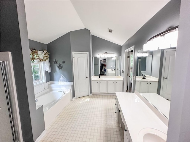 bathroom with two vanities, lofted ceiling, and a bath