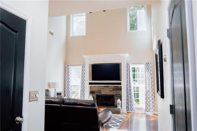 living room featuring a stone fireplace, a high ceiling, wood finished floors, and baseboards
