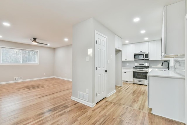 kitchen featuring light hardwood / wood-style flooring, backsplash, white cabinets, appliances with stainless steel finishes, and ceiling fan