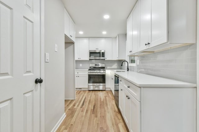 kitchen with sink, white cabinets, light hardwood / wood-style flooring, decorative backsplash, and appliances with stainless steel finishes