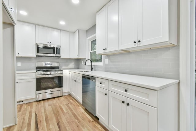 kitchen with sink, white cabinets, light wood-type flooring, and appliances with stainless steel finishes