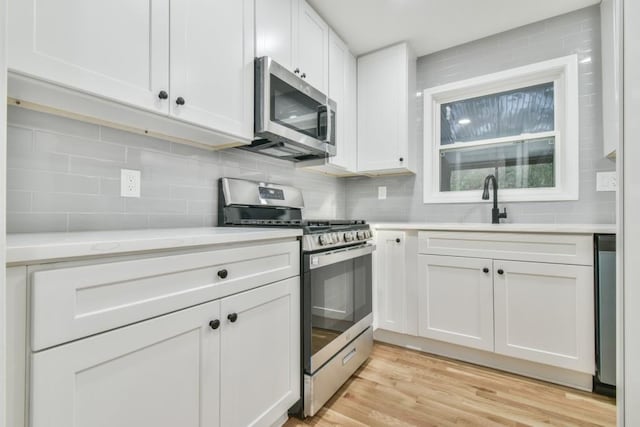 kitchen with appliances with stainless steel finishes, light hardwood / wood-style floors, sink, white cabinets, and tasteful backsplash