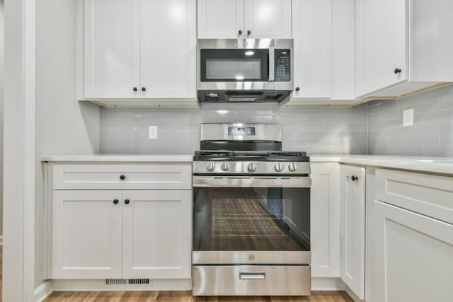 kitchen with stainless steel appliances, white cabinets, decorative backsplash, and light hardwood / wood-style flooring