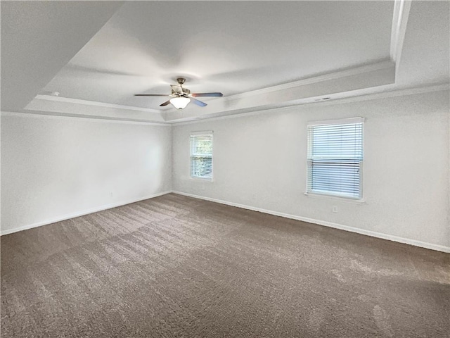 spare room featuring a tray ceiling, baseboards, crown molding, and dark colored carpet