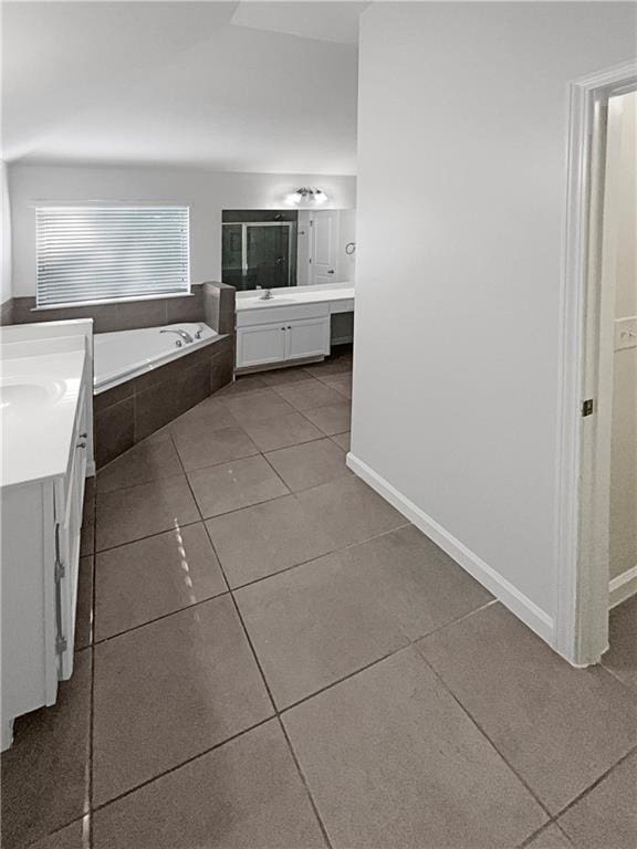 bathroom featuring baseboards, two vanities, tile patterned floors, a sink, and a bath