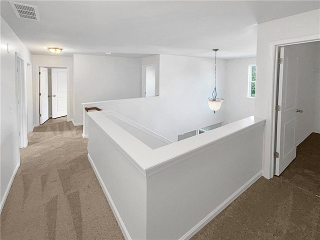 hallway with carpet, baseboards, visible vents, and an upstairs landing