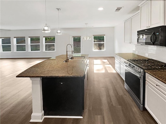 kitchen with black microwave, a kitchen island with sink, white cabinets, dark stone countertops, and stainless steel range with gas stovetop