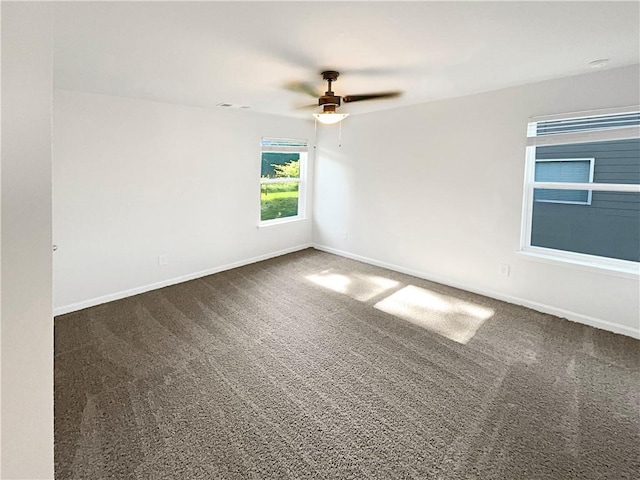 empty room with visible vents, dark colored carpet, a ceiling fan, and baseboards