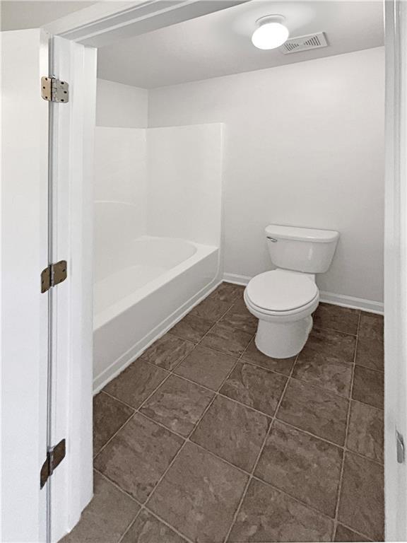 bathroom featuring tile patterned flooring, toilet, visible vents, baseboards, and a tub