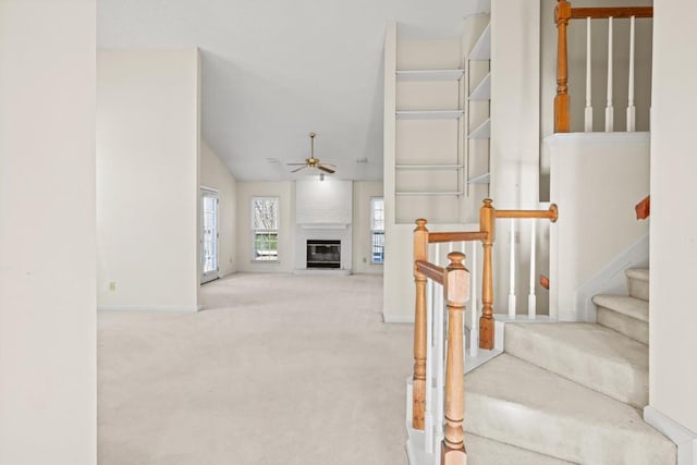 stairs with ceiling fan, lofted ceiling, carpet, and a brick fireplace