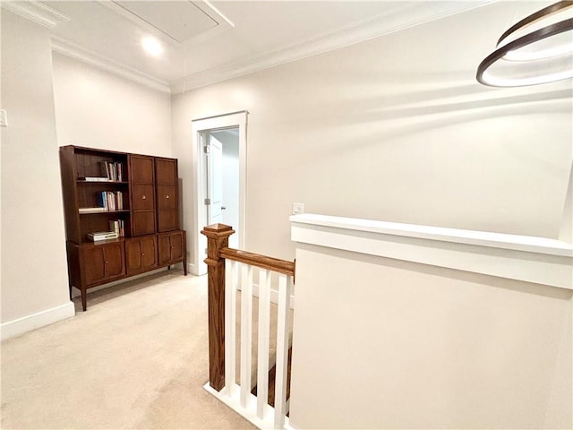 corridor with an upstairs landing, attic access, light colored carpet, ornamental molding, and baseboards