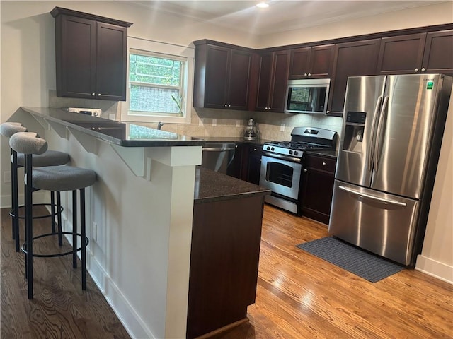 kitchen featuring appliances with stainless steel finishes, a peninsula, a kitchen bar, dark brown cabinetry, and light wood-style flooring