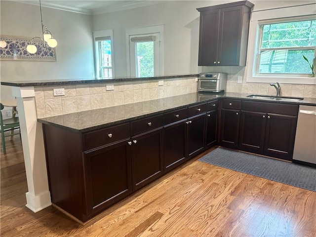 kitchen featuring a sink, light wood finished floors, dishwasher, dark stone counters, and a peninsula
