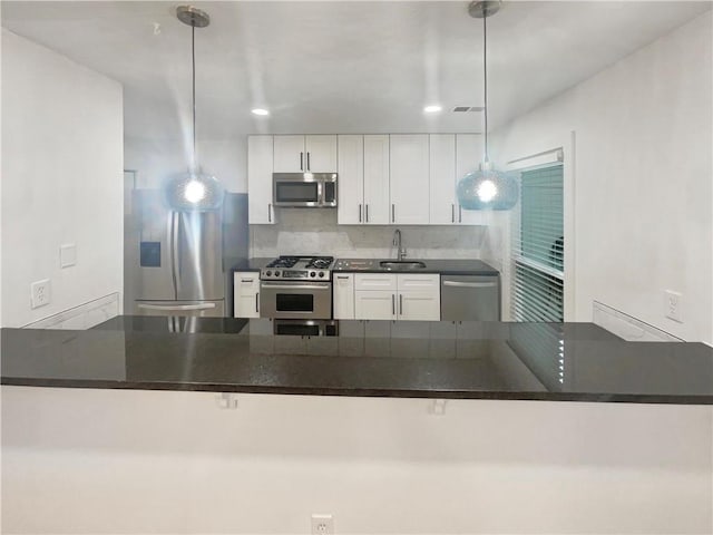 kitchen featuring a peninsula, white cabinets, appliances with stainless steel finishes, dark countertops, and pendant lighting