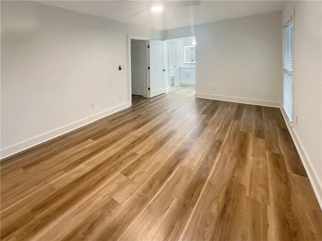 empty room with wood finished floors, a ceiling fan, and baseboards