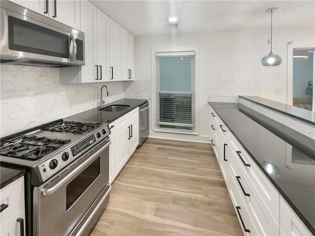 kitchen with a sink, white cabinetry, light wood-style floors, appliances with stainless steel finishes, and decorative light fixtures