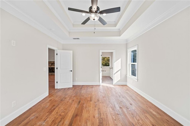 empty room with ceiling fan, a raised ceiling, ornamental molding, and light hardwood / wood-style flooring