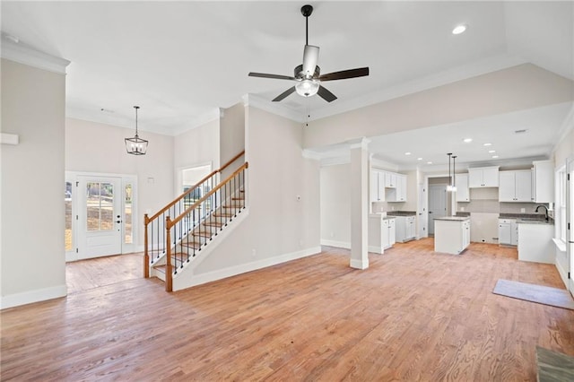 unfurnished living room with ornamental molding, sink, light hardwood / wood-style flooring, and ceiling fan with notable chandelier