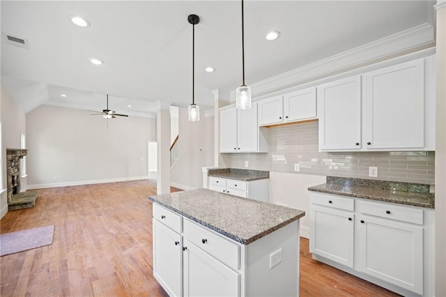 kitchen featuring a kitchen island, backsplash, light hardwood / wood-style floors, pendant lighting, and white cabinets