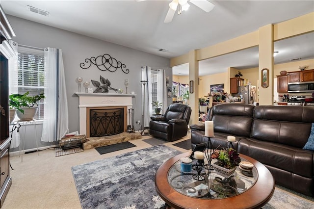 living area featuring visible vents, light carpet, ceiling fan, and a fireplace with raised hearth