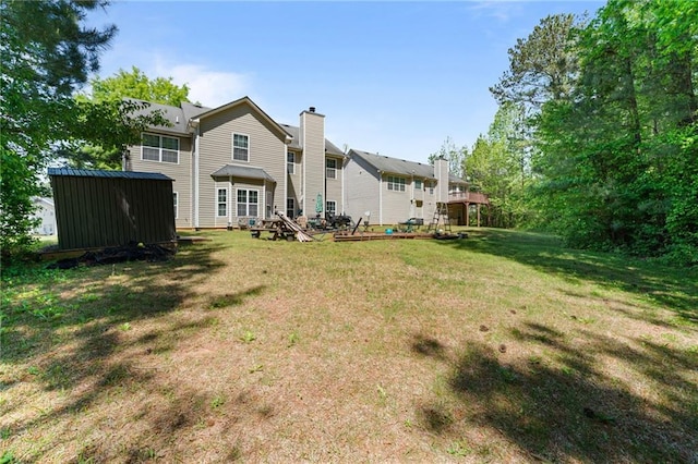 back of property with an outdoor structure, a lawn, a storage unit, and a chimney