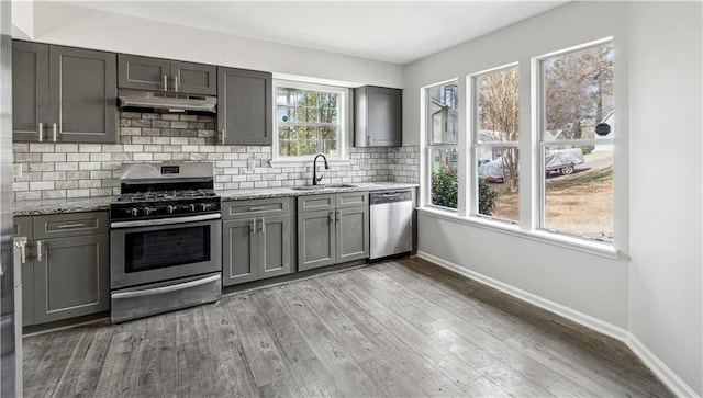 kitchen featuring sink, hardwood / wood-style flooring, stainless steel appliances, light stone countertops, and decorative backsplash