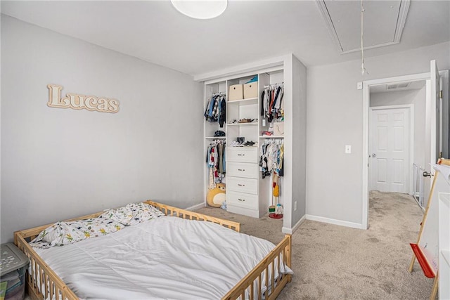 carpeted bedroom with a closet, attic access, and baseboards