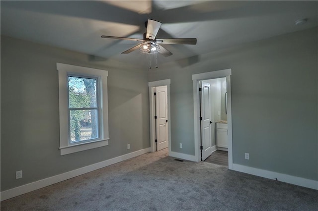 unfurnished bedroom featuring carpet, visible vents, ensuite bathroom, a ceiling fan, and baseboards