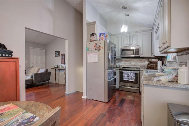 kitchen featuring appliances with stainless steel finishes, dark wood-type flooring, sink, hanging light fixtures, and vaulted ceiling