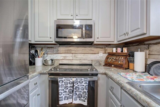 kitchen with backsplash, white cabinetry, light stone counters, and appliances with stainless steel finishes