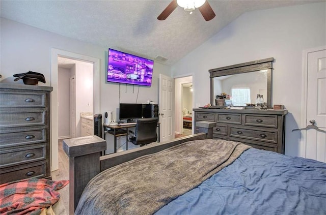 bedroom with lofted ceiling, a textured ceiling, ensuite bath, and ceiling fan