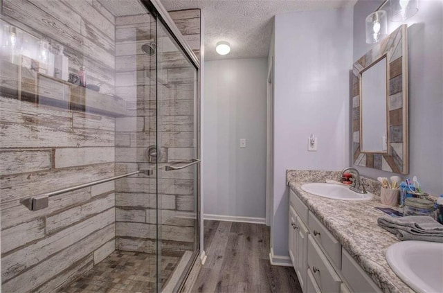 bathroom with wood-type flooring, a textured ceiling, a shower with shower door, and vanity