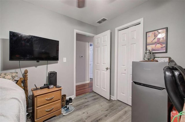 bedroom featuring a closet, ceiling fan, light hardwood / wood-style flooring, and stainless steel fridge