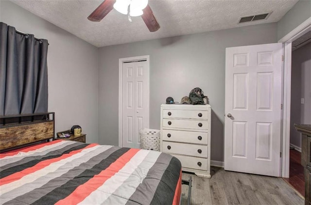 bedroom with a textured ceiling, light hardwood / wood-style flooring, a closet, and ceiling fan