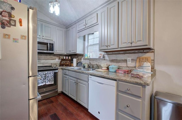 kitchen featuring a textured ceiling, lofted ceiling, dark wood-type flooring, stainless steel appliances, and sink