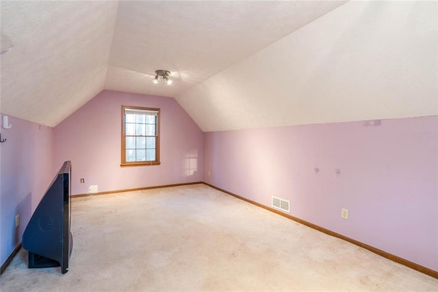 bonus room with vaulted ceiling, light colored carpet, and a textured ceiling