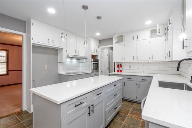 kitchen with sink, hanging light fixtures, a kitchen island, decorative backsplash, and oven