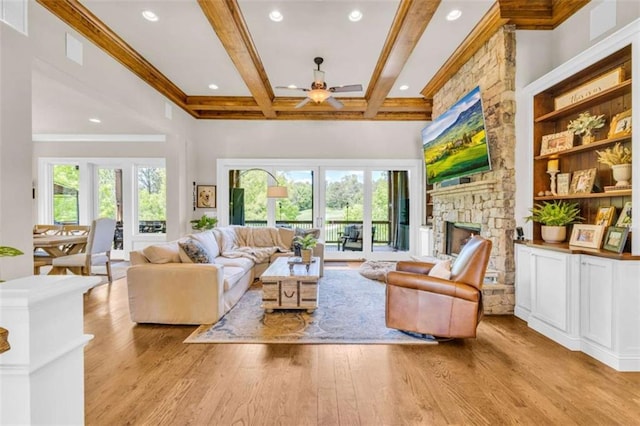 living room featuring light hardwood / wood-style flooring, ceiling fan, a fireplace, beamed ceiling, and plenty of natural light