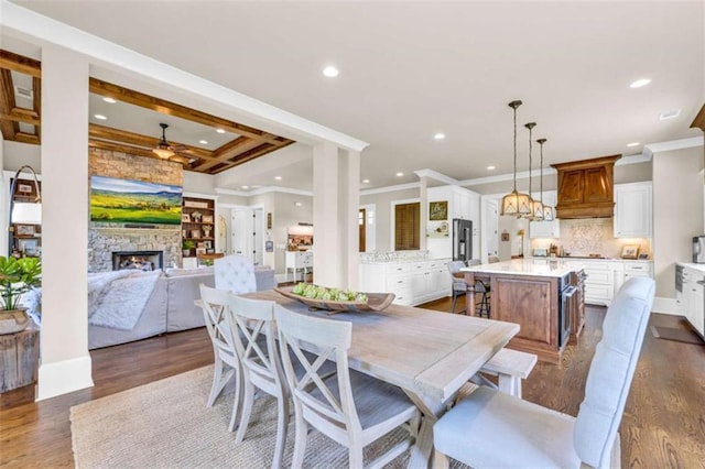 dining space with ceiling fan, a stone fireplace, ornamental molding, and dark wood-type flooring