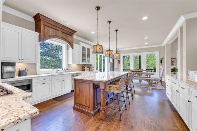 kitchen featuring decorative backsplash, light stone countertops, stainless steel dishwasher, a kitchen island, and white cabinetry