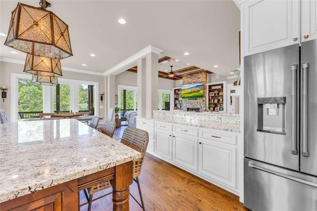 kitchen with a stone fireplace, crown molding, high quality fridge, white cabinetry, and a breakfast bar area