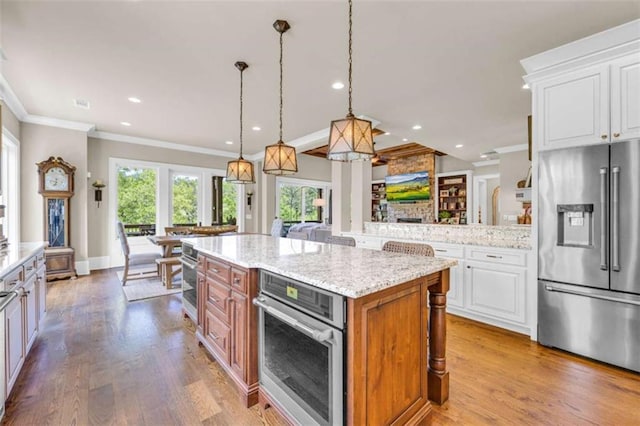 kitchen featuring light stone countertops, white cabinetry, hanging light fixtures, stainless steel appliances, and a kitchen island