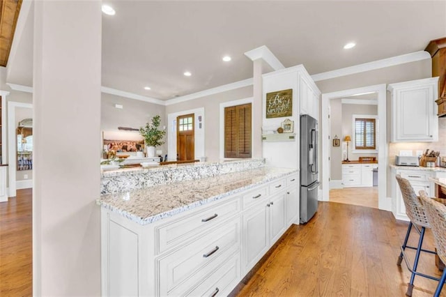 kitchen featuring light hardwood / wood-style flooring, plenty of natural light, light stone counters, white cabinetry, and stainless steel refrigerator