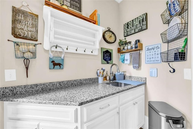 kitchen featuring light stone counters, white cabinetry, and sink