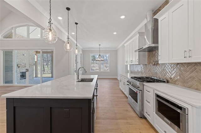 kitchen with tasteful backsplash, wall chimney exhaust hood, a kitchen island with sink, stainless steel appliances, and a sink