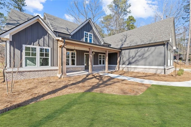 view of front of home featuring board and batten siding, roof with shingles, brick siding, and a front lawn